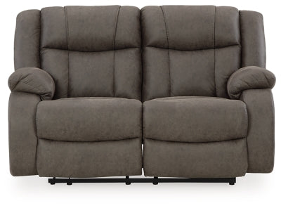 Ashley Furniture First Base reclining loveseat showing plush fabric, wide armrests, and a comfortable reclining position.