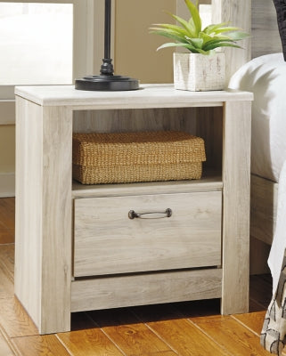 Ashley Furniture Bellaby Nightstand with drawer and open shelf, dark wood finish, modern design, placed beside a bed.