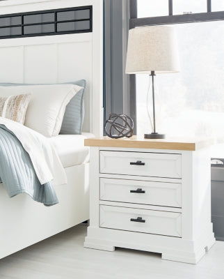 Ashbryn nightstand by Ashley Furniture with a dark wood finish and sleek drawer handles, shown in a modern bedroom setting.