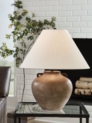 Ashley Furniture Ferrilby table lamp with a ceramic base and fabric shade, shown on a wooden table in a cozy living room setting.