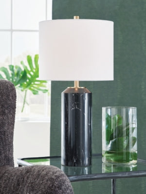Ashley Furniture Hanzila table lamp with a sleek design and fabric shade, shown on a wooden table in a modern living room setting.